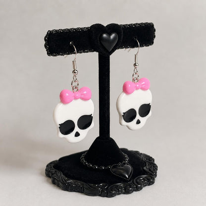 Glossy white skull charm detail with oversized black eyes on bow earrings